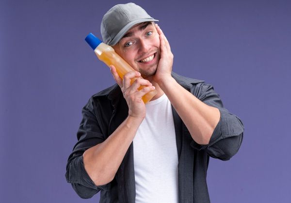 Happy man with a bottle of vinegar in his hand putting it on his face representing its benefits