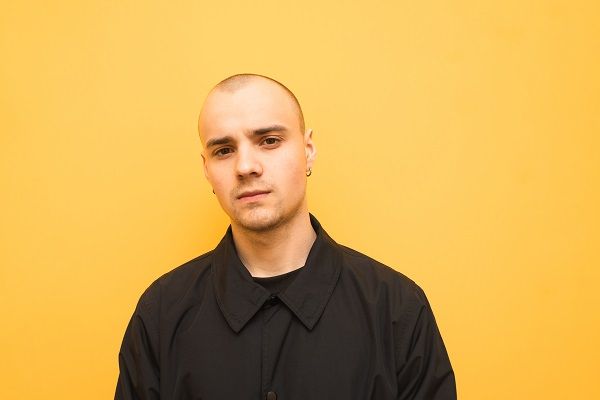 Stylish young man with a bald head wearing black jacket poses on