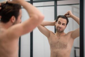 Man in front of mirror combing his hair with a smiling face due to the effectiveness of Minoxidil