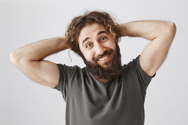 Happy charismatic middle-eastern man with beard, smiling and combing hair