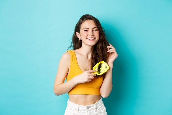Beautiful young woman smiling, brushing healthy long hair with hairbrush