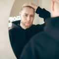 Man in front of the mirror touching his hair with the onset of androgenetic alopecia