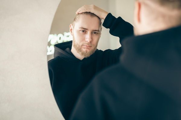 Man in front of the mirror touching his hair with the onset of androgenetic alopecia